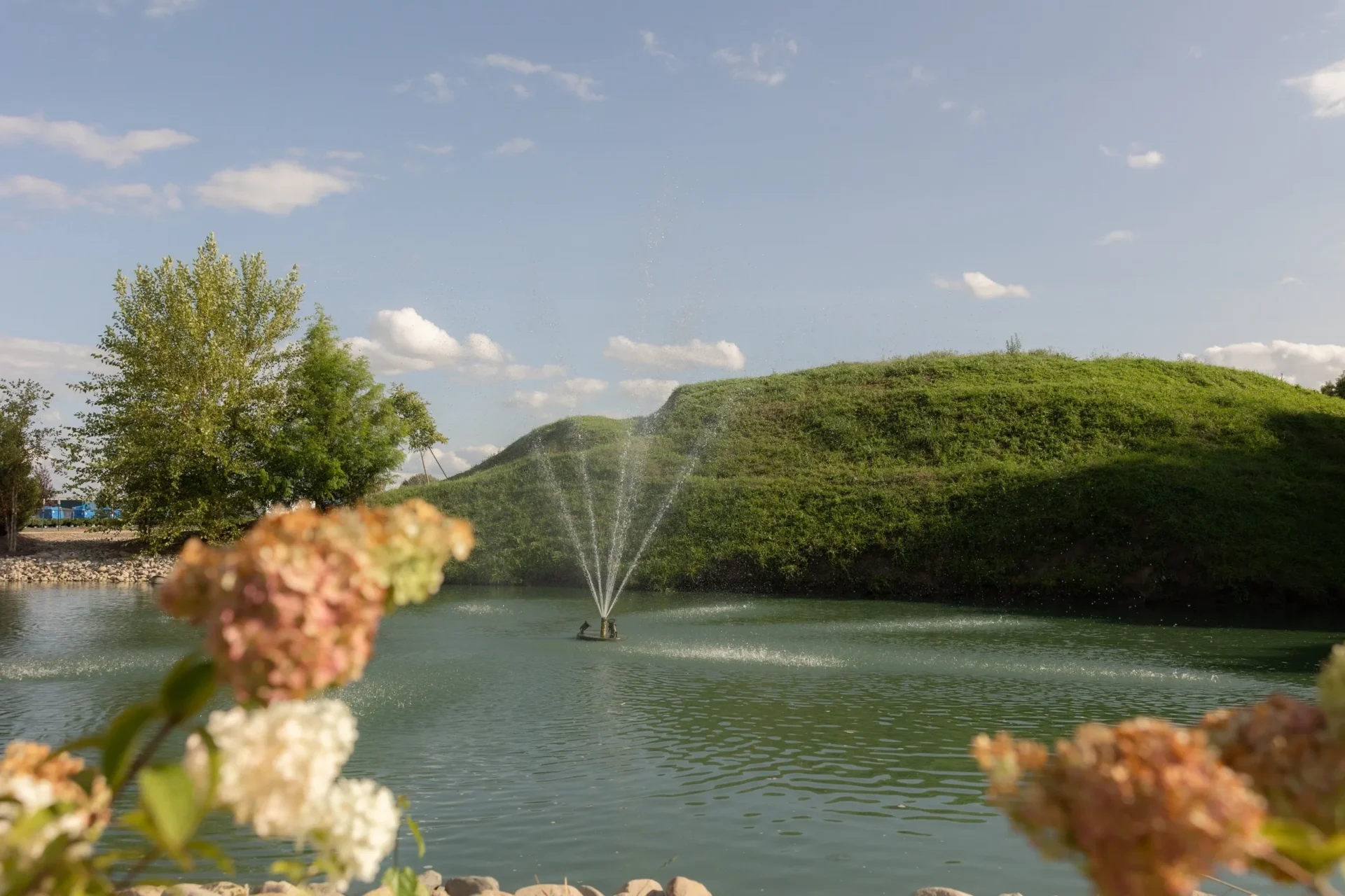Fountain spraying in pond with grassy hill